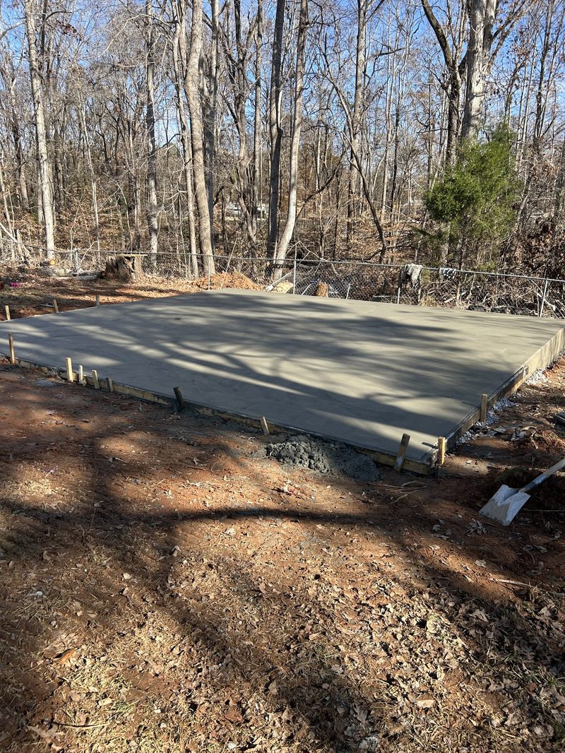 Freshly poured concrete pad with wooden forms in residential backyard